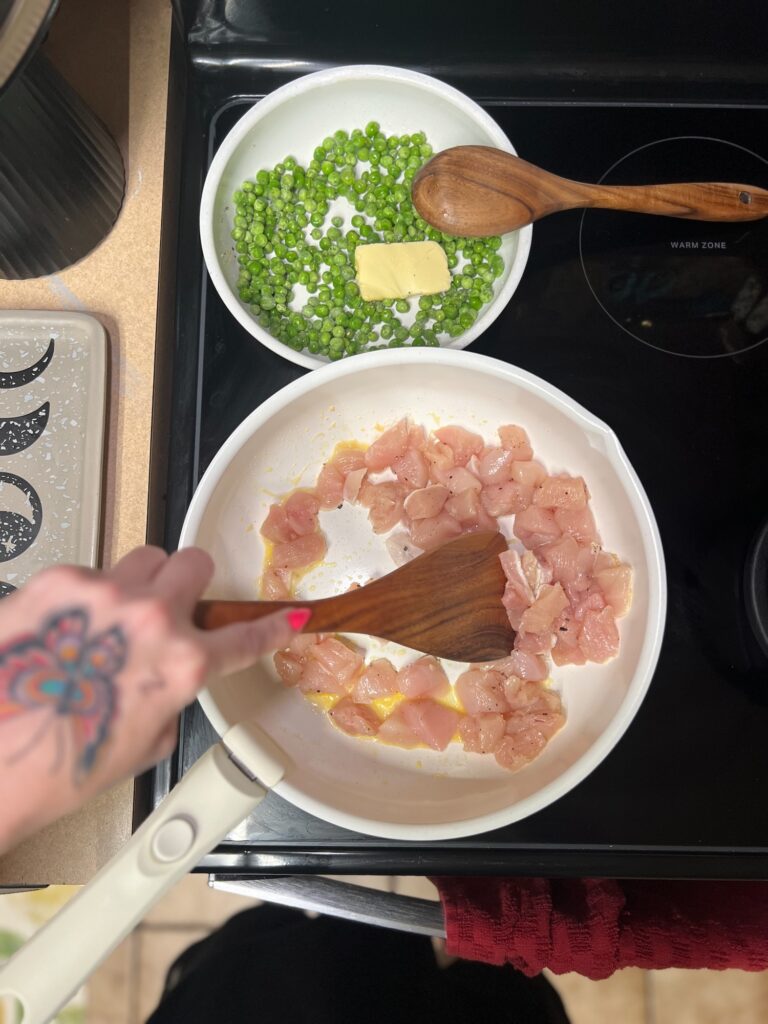 Easy family dinner in progress with chicken and peas cooking in a skillet on the stove in a home kitchen.